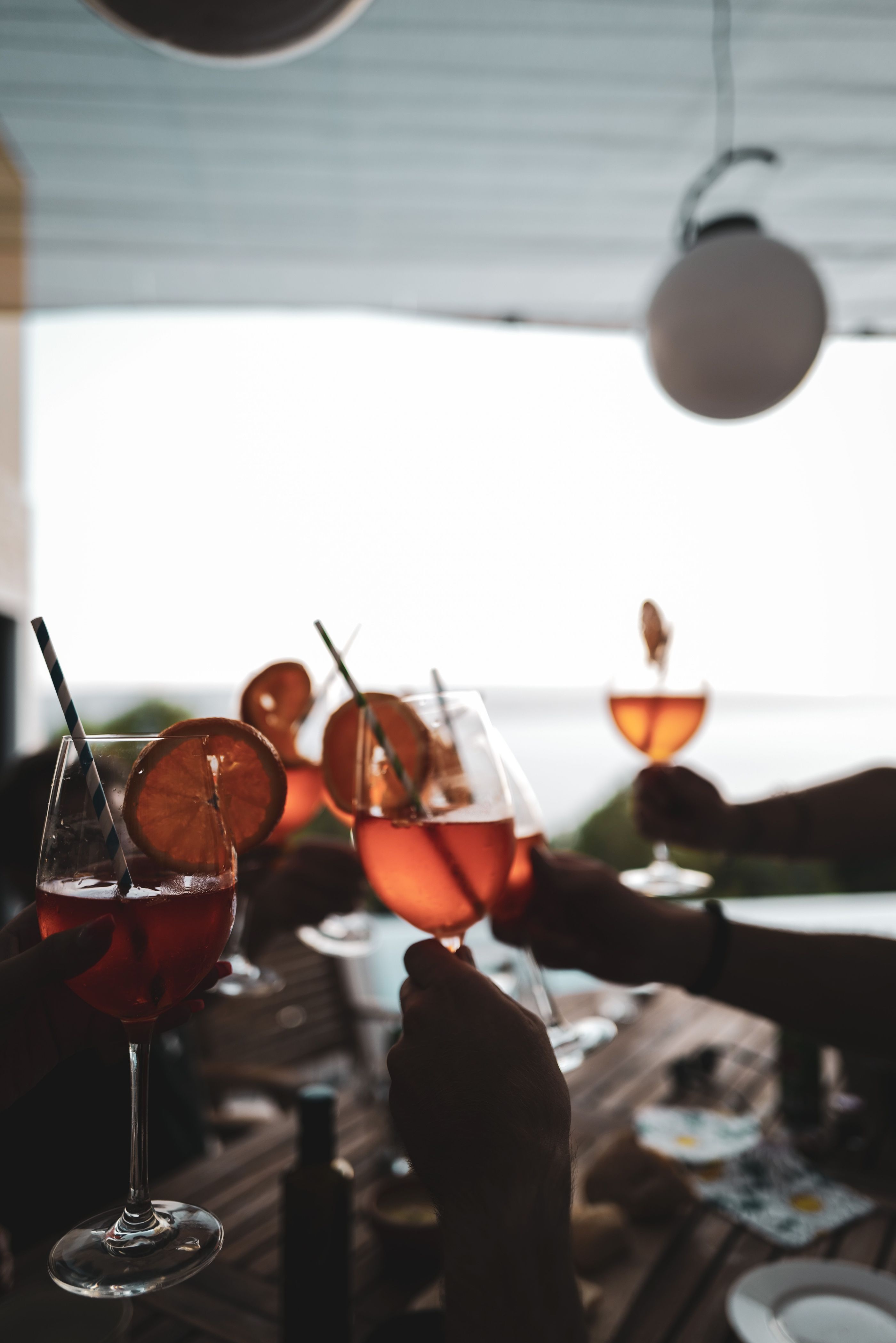 A group of friends bringing their drinks together. They are sitting at a table overlooking the ocean.