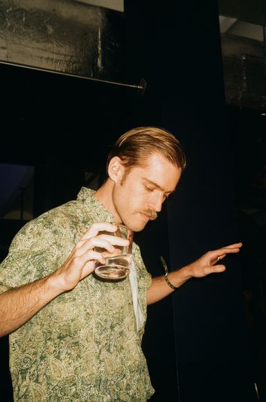 A man in a patterned green shirt dancing. He is holding a drink in his right hand.